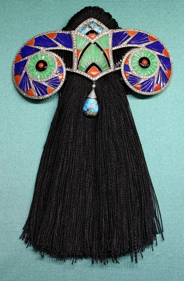 A Boucheron Art Deco corsage ornament: A corsage ornament of palladium gold, lapis lazuli, coral, jade, onyx and turquoise made by Boucheron in 1925, the year of the Paris exhibition that gave Art Deco its name.