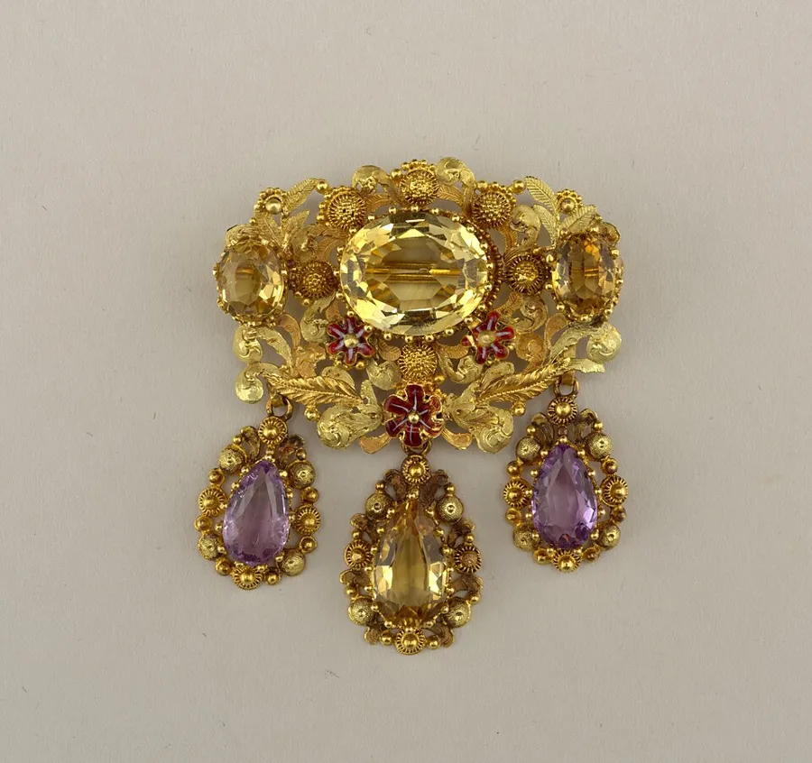 A French gold brooch with citrines and amethysts: A gold brooch made in France about 1820 to 1840, with a large yellow citrine at its centre and drops of citrine and amethyst.