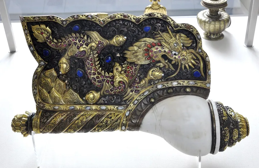 A Tibetan conch-shell trumpet: A conch-shell trumpet (dung-dkar) mounted in copper and gilt copper alloy set with semi-precious stones, with a dragon on its metal flange, 44 cm long, used in a monastery orchestra.