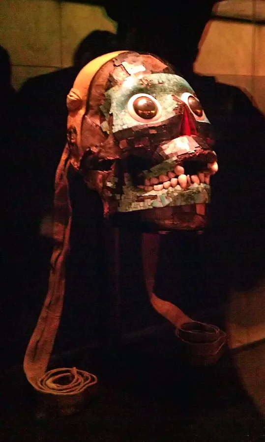 The mask of Tezcatlipoca: A human skull covered in bands of turquoise and black lignite mosaic, with eyes of pyrite and shell, Aztec or Mixtec, 15th to 16th century.