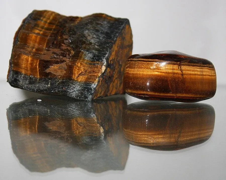 Tiger’s eye, rough and polished: A rough piece beside a polished one, showing how the dull, fibrous rock turns to rolling gold light when it is cut smooth.
