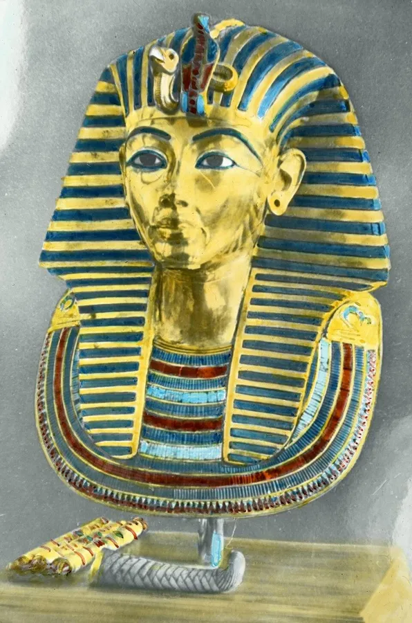 Tutankhamun’s gold mask: The funeral mask of Tutankhamun, solid gold inlaid with lapis lazuli, carnelian, quartz and coloured glass, about 1323 BC, in an early hand-coloured postcard.