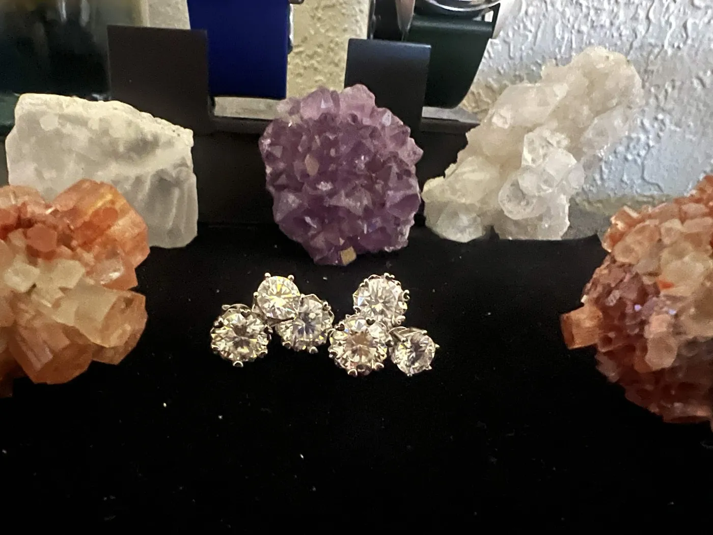Moissanite studs on black cloth in front of amethyst and aragonite crystal specimens