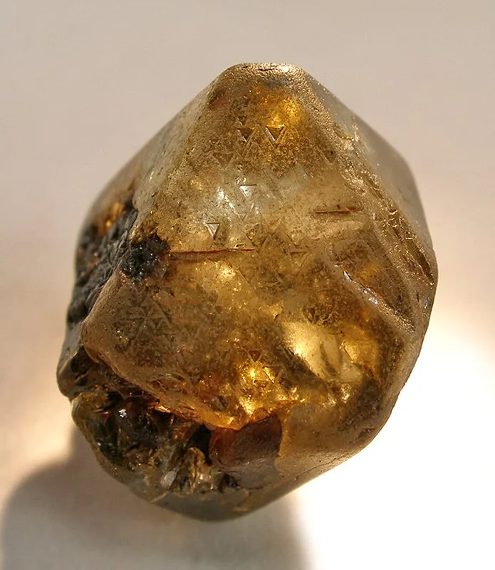 A natural diamond crystal: an octahedron, the shape diamond grows in, with a frosted, etched skin.