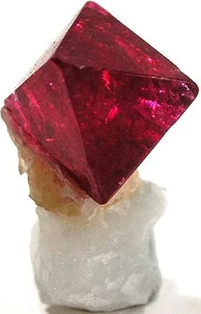 A red spinel octahedron on white marble, Mogok, Myanmar. Spinel grows in the same marble as ruby, which is how the two got confused.